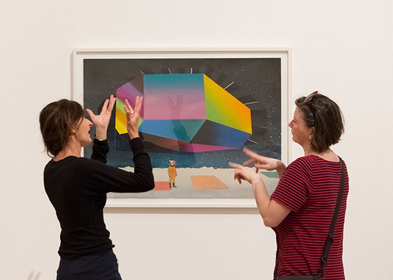Two women standing infront of the painting and speaking sign-language